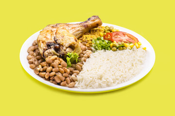 rice and beans dish, large roasted chicken thigh, chopped tomato salad with corn and peas, on isolated yellow background, traditional brazilian meal