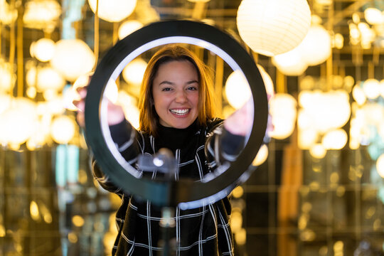 Smiling woman holding ring light by lanterns