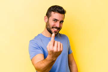 Young caucasian man isolated on yellow background pointing with finger at you as if inviting come closer.