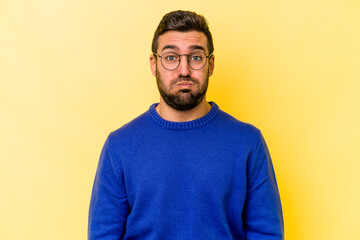 Young caucasian man isolated on yellow background blows cheeks, has tired expression. Facial expression concept.