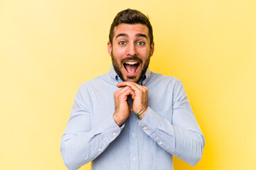 Young caucasian man isolated on yellow background praying for luck, amazed and opening mouth looking to front.