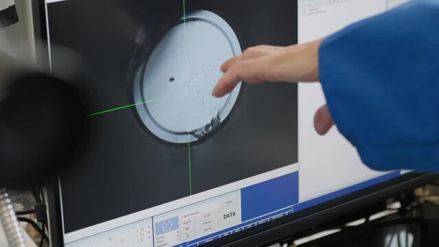 Hand pointing to cross section of glass fiber under microscope on screen in laboratory