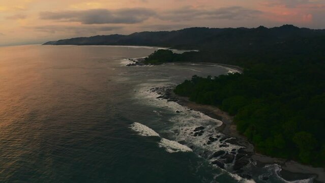 Aerial view around waves hitting rocks at the Playa Mal Pa&iacute;s beach, evening in Costa Rica - orbit, drone shot