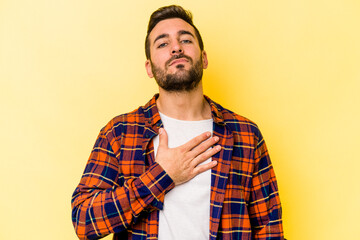 Young caucasian man isolated on yellow background taking an oath, putting hand on chest.