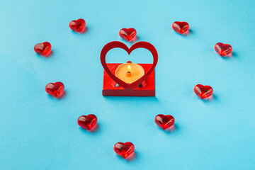 On a blue background, a burning candle in a frame in the shape of a heart decorated with hearts with pebbles.