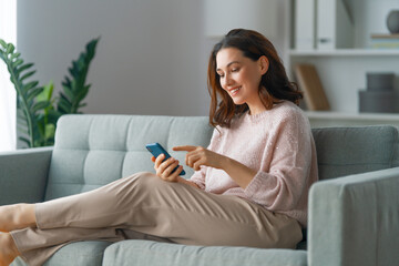 woman is using a phone sitting on a sofa