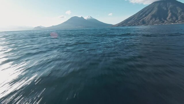 Fast flying close to lake Atilan water surface revealing volcano mountain with cloud cap. Aerial fpv view