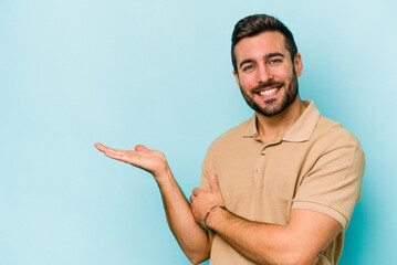 Young caucasian man isolated on blue background showing a copy space on a palm and holding another...