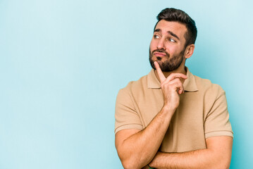 Young caucasian man isolated on blue background looking sideways with doubtful and skeptical expression.