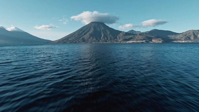 Volcano peak covered with cloud cap, aerial FPV flying towards over lake Atilan