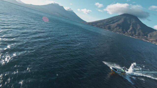 Boat speeding on Atilan lake with massive volcano in background, aerial FPV view