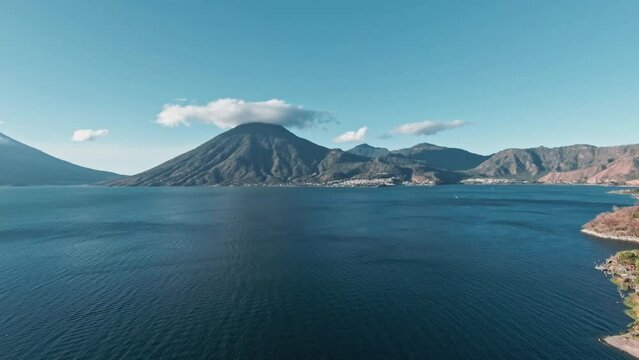 Vibrant blue lake Atilan and high mountain range with cloud cap, aerial ascend view