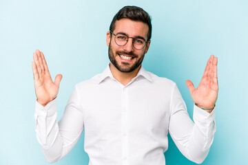 Naklejka premium Young caucasian man isolated on blue background holding something little with forefingers, smiling and confident.