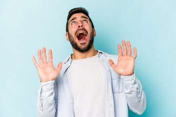 Young caucasian man isolated on blue background screaming to the sky, looking up, frustrated.
