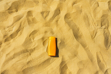 Sunscreen - A bottle of sunscreen with no logo lying on the textured sand background.