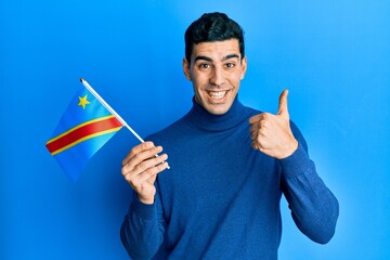 Handsome hispanic man holding democratic republic of the congo flag smiling happy and positive,...