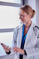 Portrait Of Mature Female Doctor Wearing White Coat Looking At Digital Tablet In Hospital