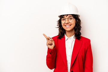 Young architect hispanic woman with helmet isolated on white background smiling and pointing aside, showing something at blank space.
