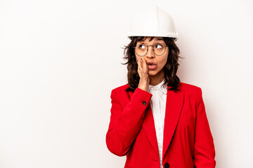 Young architect hispanic woman with helmet isolated on white background is saying a secret hot braking news and looking aside