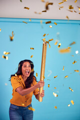 Excited Mature Woman Celebrates Winning Firing Gold Confetti Canon In Studio Against Blue Background