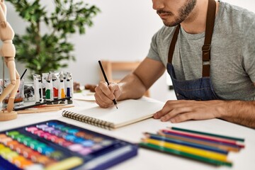 Young hispanic artist man with serious expression painting at art studio.