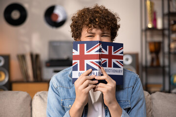 A teenager with curly hair sits focused in a room studying for an English exam. A boy in a blue jean shirt prepares for an English job interview. - obrazy, fototapety, plakaty