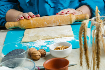 Women's hands roll out dough. Gomentash biscuits with poppy seeds, traditional for the Jewish holiday of Purim, on the table where the menorah stands.