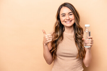 Young caucasian woman holding a bottle of water isolated on beige background smiling and raising thumb up