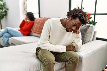 Young interracial couple on problems with sad expression sitting on the sofa at home.