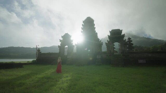 Magical bright sunlight behind Pura Ulun Danu Tamblingan temple with woman in red dress