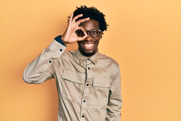Young african american man wearing casual clothes and glasses doing ok gesture with hand smiling, eye looking through fingers with happy face.