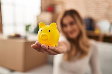 Young blonde woman smiling confident holding piggy bank at new home