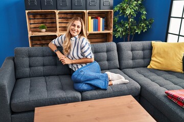 Young blonde woman smiling confident sitting on sofa at home