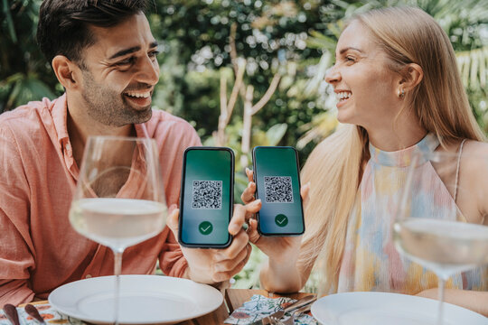 Happy couple showing QR codes on smart phones at restaurant