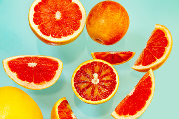 Whole and sliced juicy red oranges and grapefruits on a blue background.
