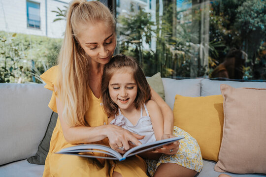 Mother and daughter reading a book sitting on sofa