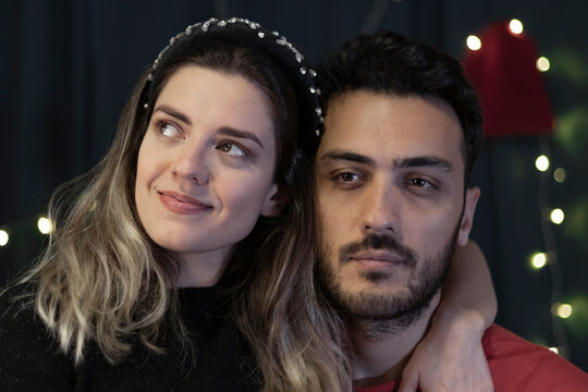 Happy girl holding hands around the neck of her boyfriend and smiling. She is looking left side. But her boyfriend is unhappy. Bokeh lights background. 