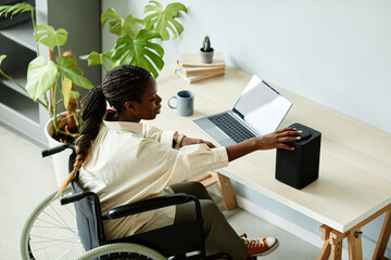 Portrait of African American woman in wheelchair using laptop while working at home office with...