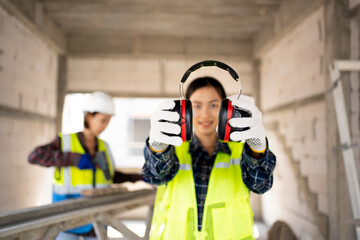 Pretty Asian Engineer,foreman Campaign to wear soundproofing equipment.Recommendations for wearing ear muffs.
Work safely with noise reduction.
a young woman using an electric screwdriver safely. - obrazy, fototapety, plakaty