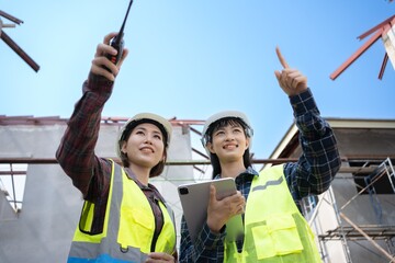 Two young Asian engineer are smiling pointing finger at a house construction project.
working the...