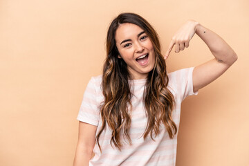 Young caucasian woman isolated on beige background person pointing by hand to a shirt copy space, proud and confident