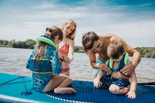 Parents fastening life jacket for their children in lake