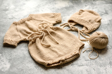 Baby knitted beige clothes on a white concrete background