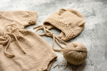 Baby knitted beige clothes on a white concrete background