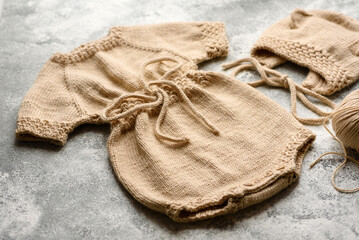 Baby knitted beige clothes on a white concrete background