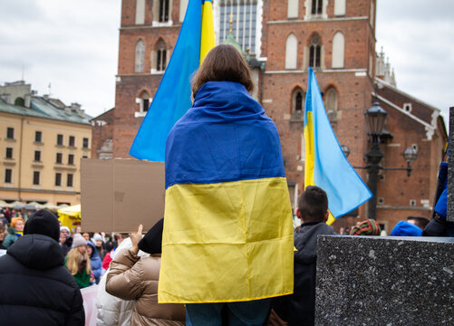Girl wearing Ukrainian flag in protest manifestation against war and Russia invasion on the Ukraine. Anti-war demonstration at Main Square Market Krakow, Poland, next to St. Mary's Basilica Kraków.