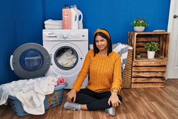 Young hispanic woman doing laundry winking looking at the camera with sexy expression, cheerful and...
