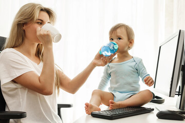 Young freelancer mother drinks coffe and her son drinks water at home office.