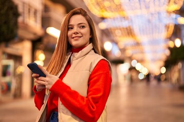 Young blonde woman smiling confident using smartphone at street