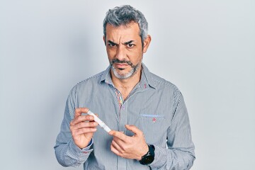 Handsome middle age man with grey hair holding glucometer device clueless and confused expression. doubt concept. - obrazy, fototapety, plakaty